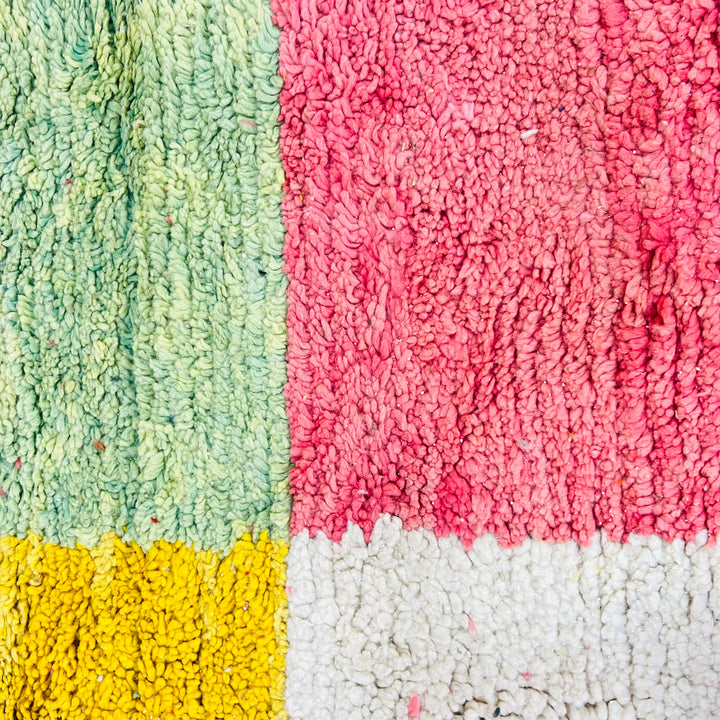 Close-up of colorful Moroccan wool rug with pink, green, yellow, and white patchwork design, perfect for boho interiors.