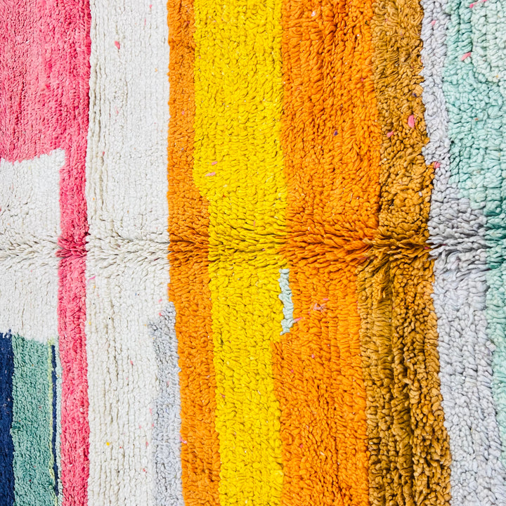 Colorful Moroccan wool rug with vibrant stripes in yellow, orange, pink, blue, and white, handwoven in a modern Berber patchwork style.