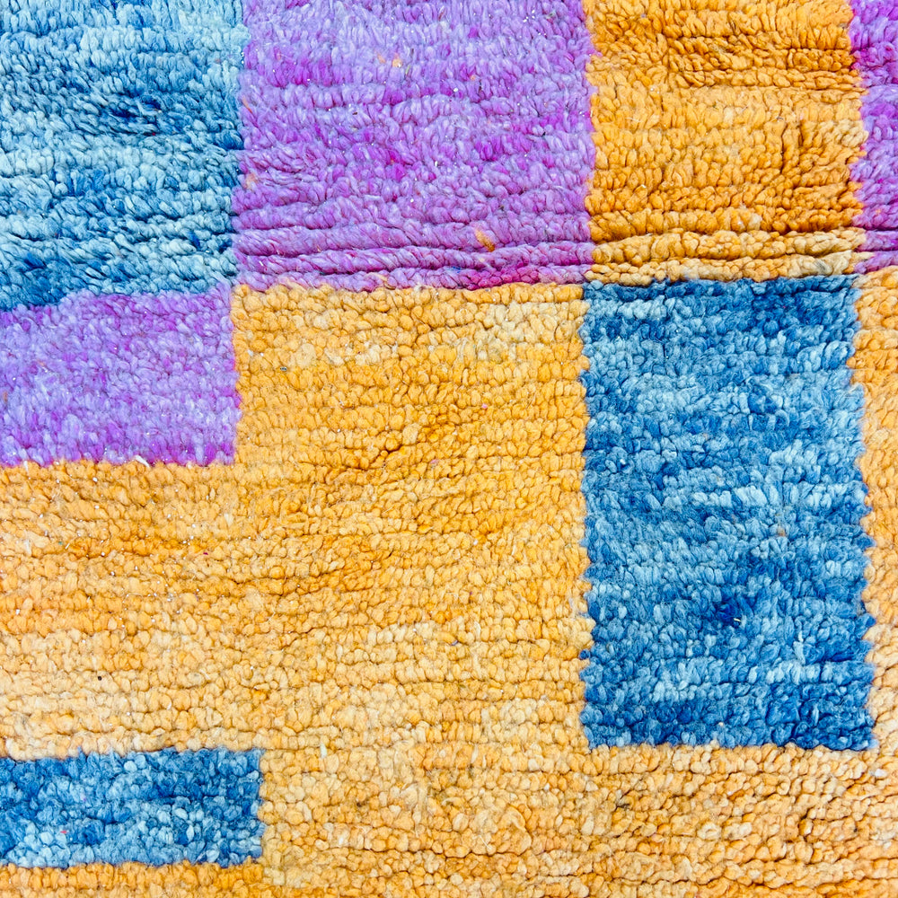 Close-up of a colorful vintage Moroccan rug with blue, purple, and orange squares, showcasing vibrant traditional patterns.