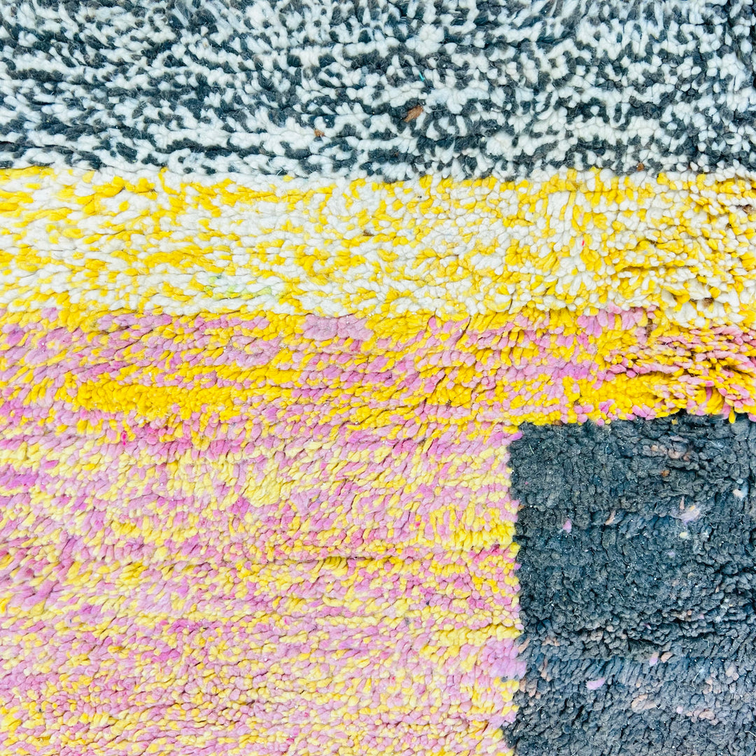 Close-up of a vibrant vintage Moroccan wool rug with pink, yellow, and black textured blocks, handcrafted by Berber artisans.