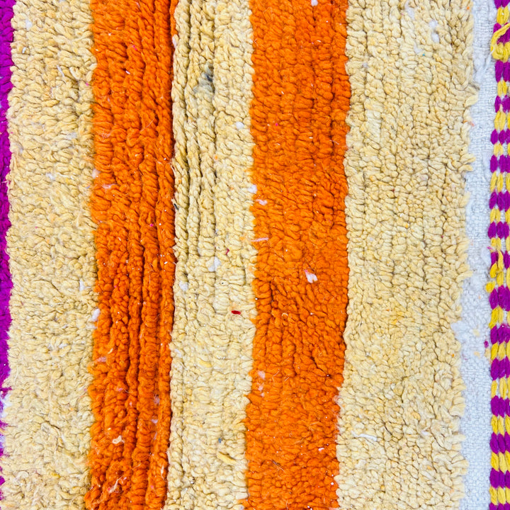 Close-up of a vibrant Moroccan wool rug with bold orange and creamy yellow stripes, perfect for bohemian decor.