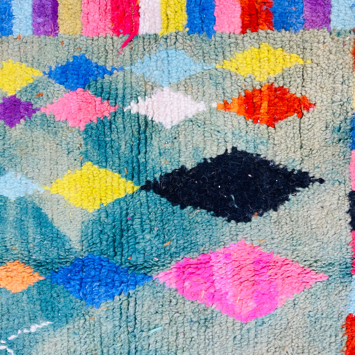 Colorful geometric vintage Moroccan rug with diamond motifs, featuring vibrant shades of pink, blue, and yellow. Handmade by Berber artisans.