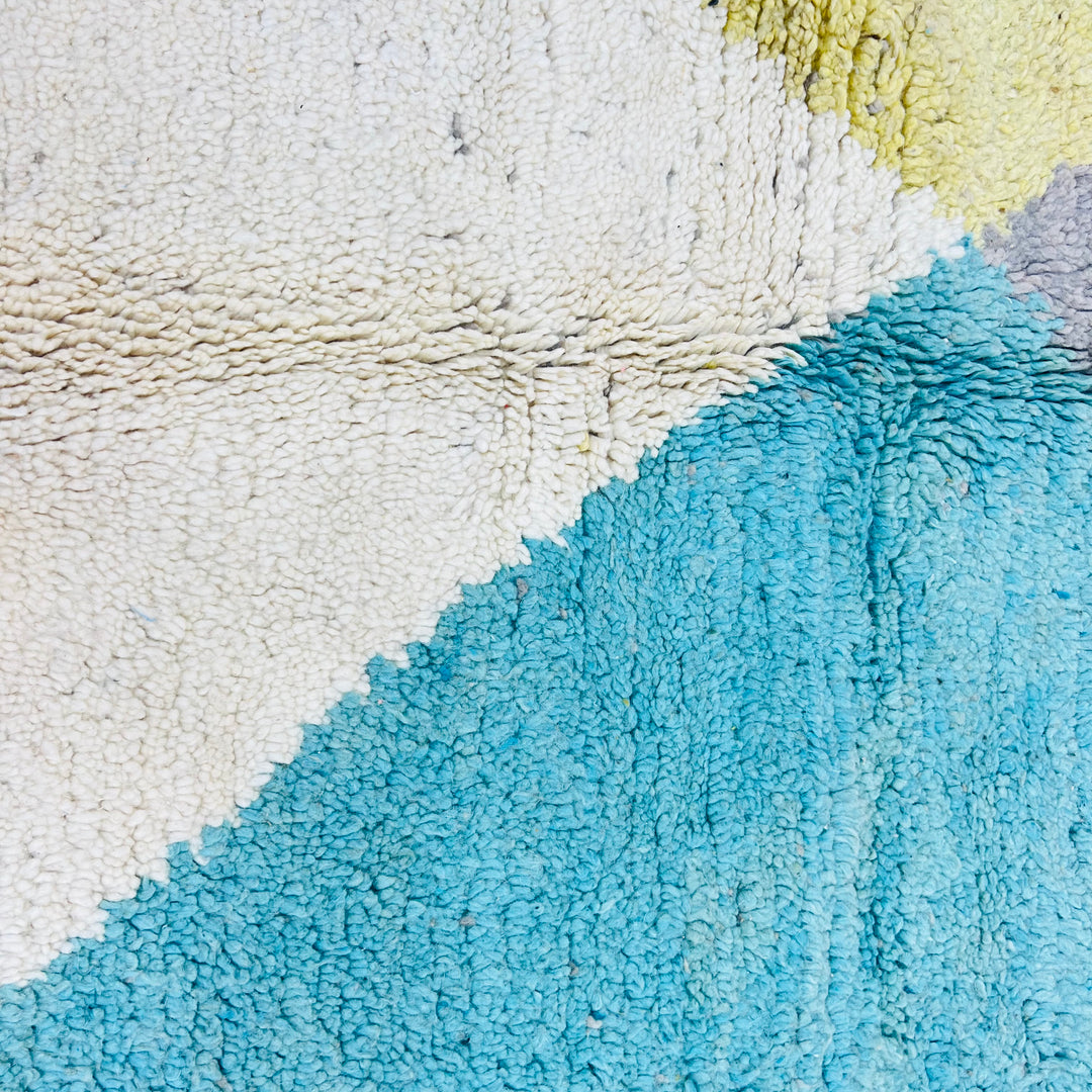 Close-up of geometric Moroccan rug in earth tones, featuring teal, beige, and mustard. Vintage handmade wool from the Atlas Mountains.