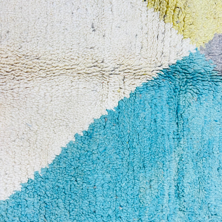 Close-up of geometric Moroccan rug in earth tones, featuring teal, beige, and mustard. Vintage handmade wool from the Atlas Mountains.