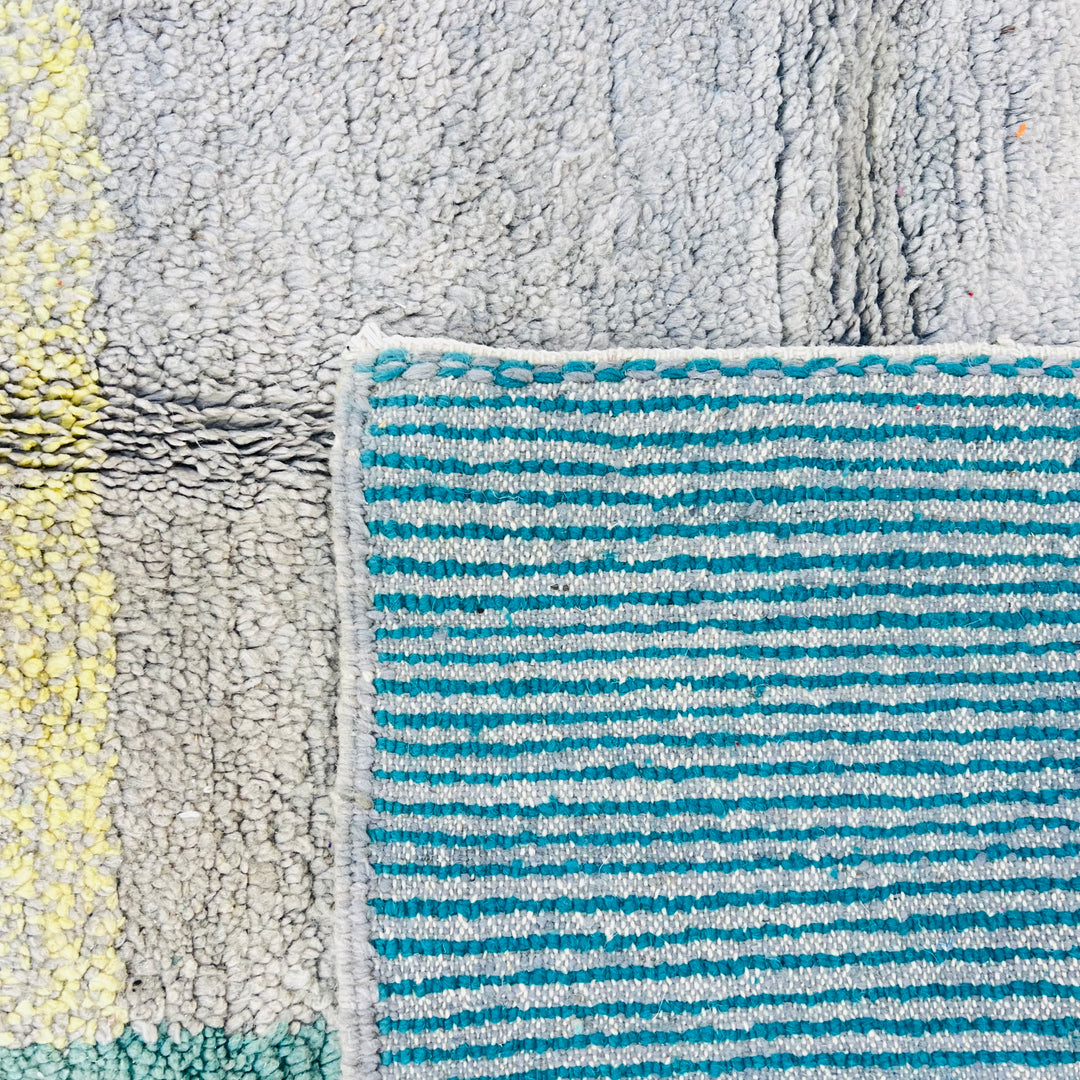Close-up of geometric Moroccan wool rug with teal, beige, and turquoise stripes. Handmade vintage design from the Atlas Mountains.