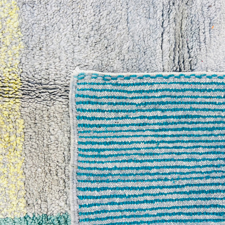 Close-up of geometric Moroccan wool rug with teal, beige, and turquoise stripes. Handmade vintage design from the Atlas Mountains.