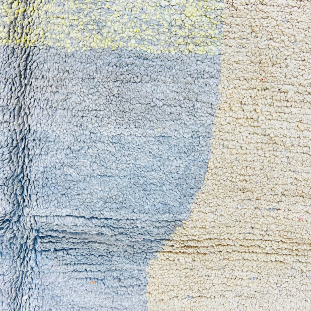 Close-up of geometric earth tone Moroccan rug with blue and beige abstract design, handmade wool texture from the Atlas Mountains.
