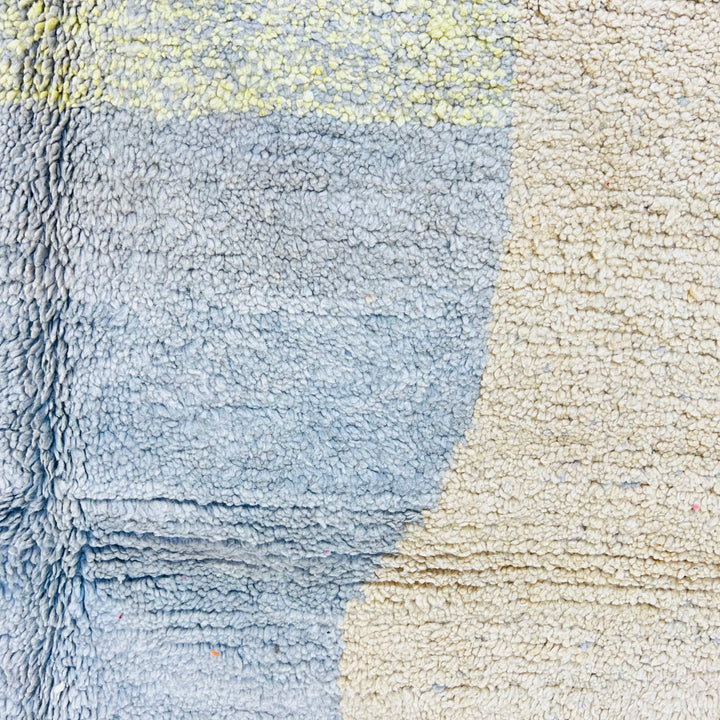 Close-up of geometric earth tone Moroccan rug with blue and beige abstract design, handmade wool texture from the Atlas Mountains.