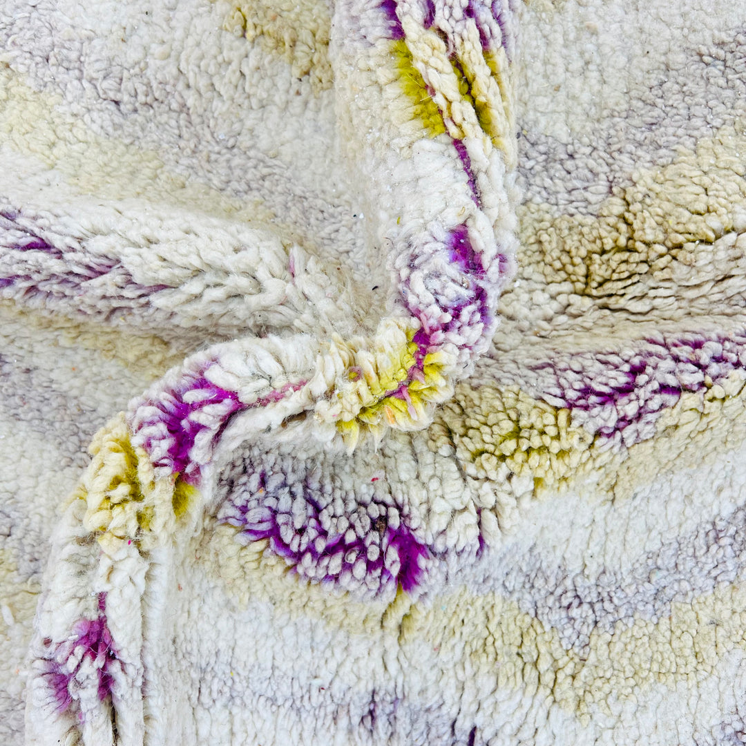 Close-up of vintage Moroccan wool rug with soft beige, lilac, and yellow accents. Handmade texture showing intricate chevron pattern.