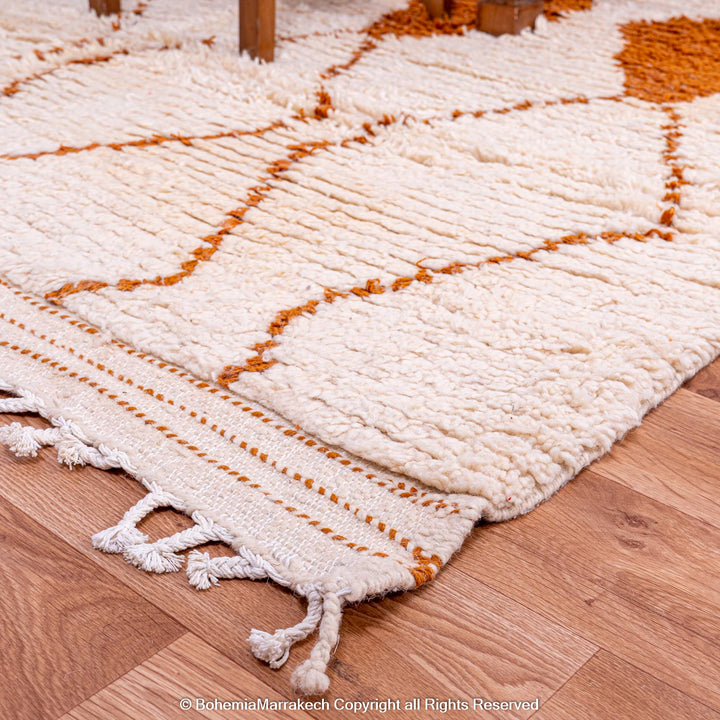 White Moroccan wool rug with rust-orange diamonds in a Beni Ourain pattern, crafted by Berber artisans. Luxurious and soft texture.