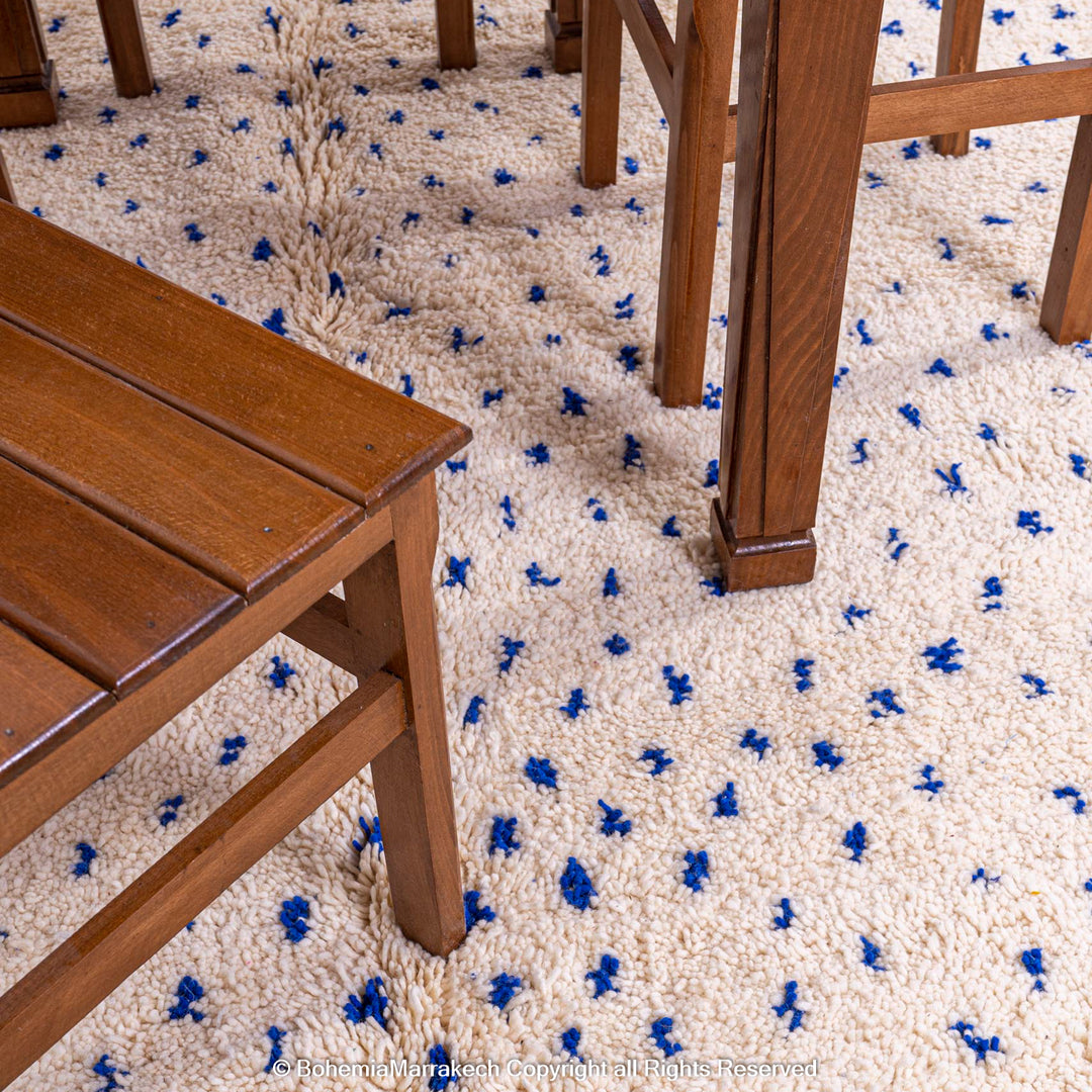 Wooden furniture on a large white Moroccan rug with blue dots, showcasing traditional Beni Ourain craftsmanship and natural wool.