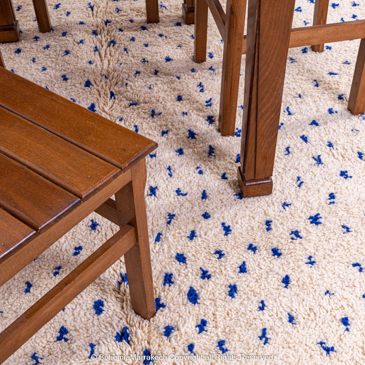 Wooden furniture on a large white Moroccan rug with blue dots, showcasing traditional Beni Ourain craftsmanship and natural wool.