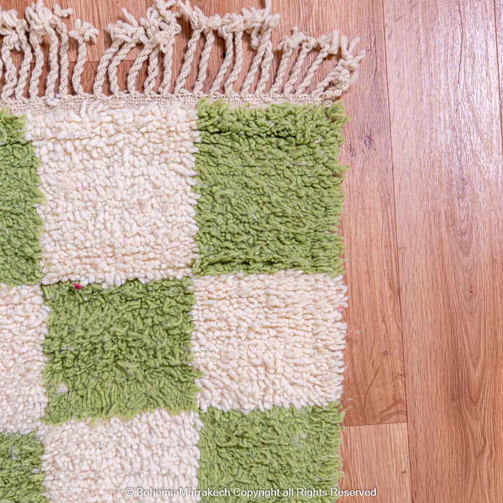 Green and white checkered Moroccan wool rug on wooden floor