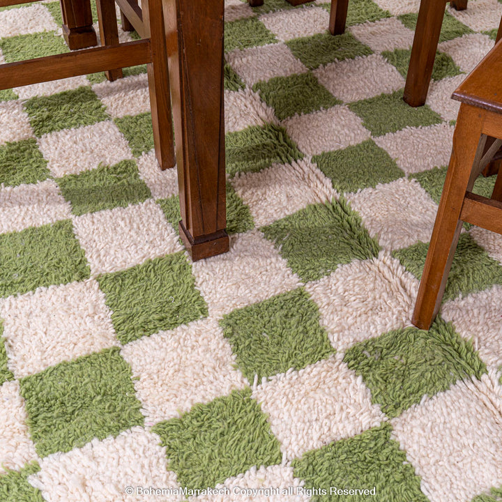 Green and white checkered Moroccan wool rug under wooden dining table, handmade by Berber artisans, adding vintage charm to decor.