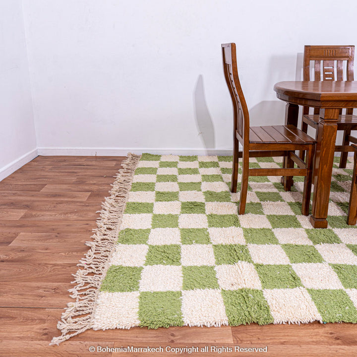 Green white checkered Moroccan wool rug in a dining area with wooden table and chairs.