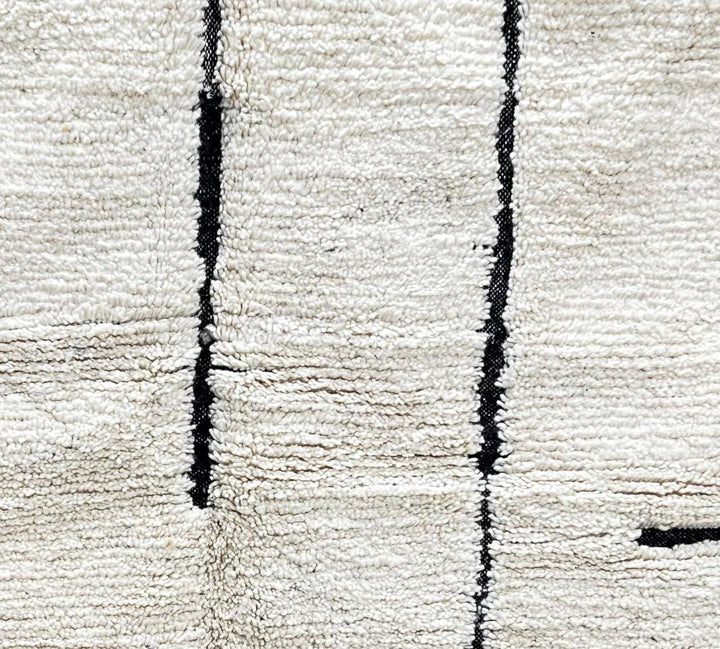 Handmade minimalist Moroccan runner rug with black linear abstract design on natural white wool background.