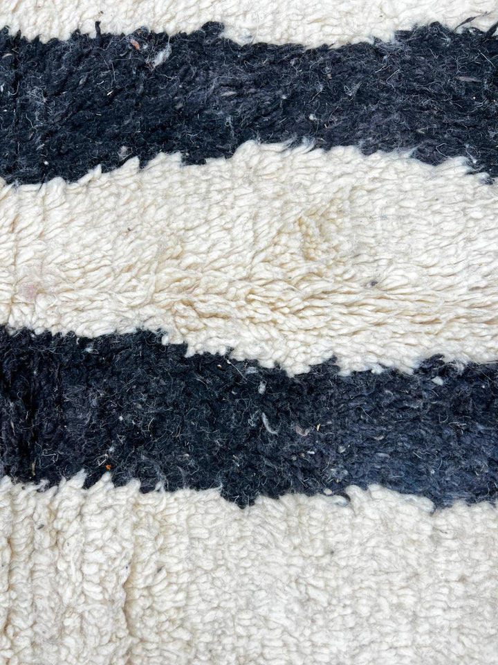 Round Moroccan wool rug with abstract black and rust lines on white background