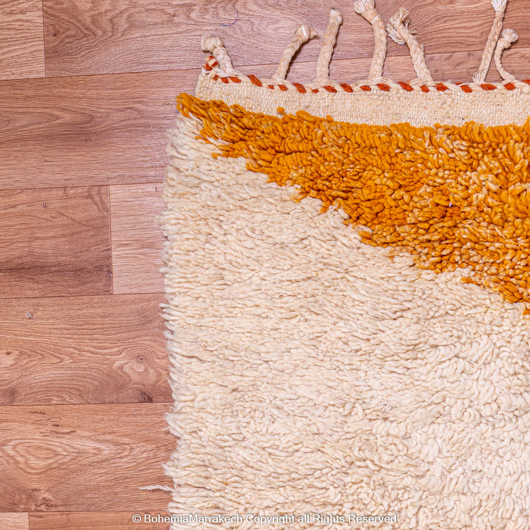 Orange and cream handmade Moroccan wool shag rug on a wooden floor, featuring traditional geometric design.