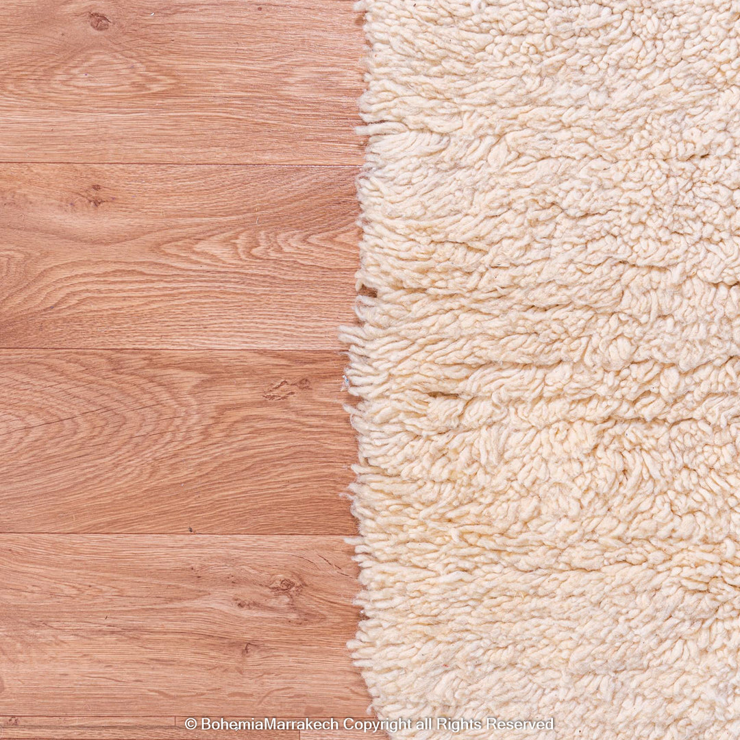 Close-up of a cream-colored Moroccan wool shag rug on wooden flooring.