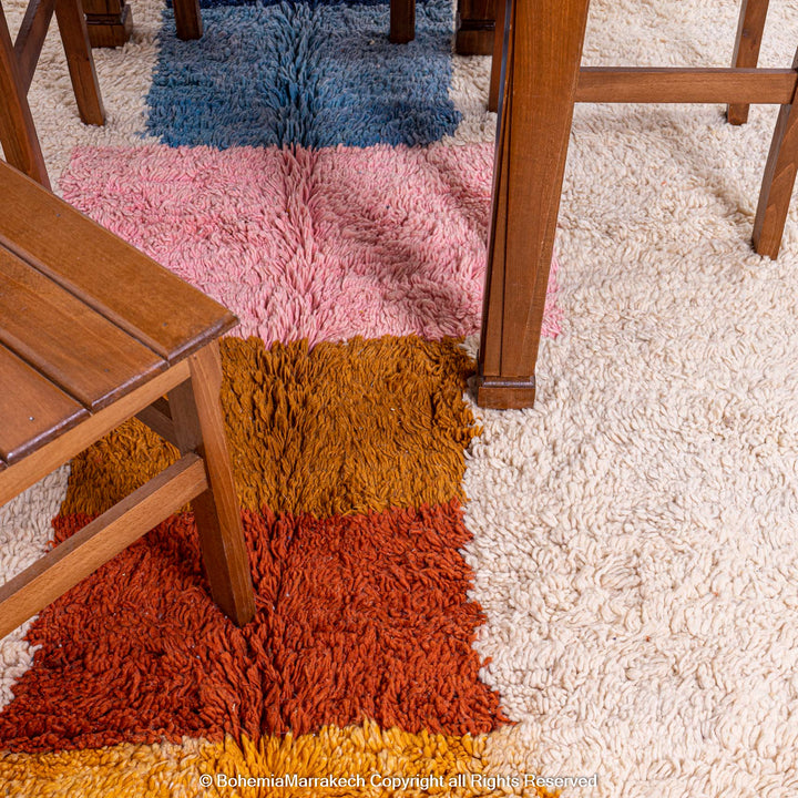 Colorful handmade Moroccan wool shag rug with geometric patterns under a wooden table, showcasing vibrant colors like pink and blue.