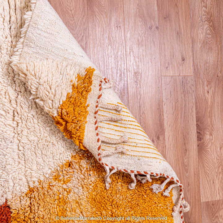 Handmade Moroccan wool shag rug with orange geometric design, showcasing artisan craftsmanship on wooden floor.