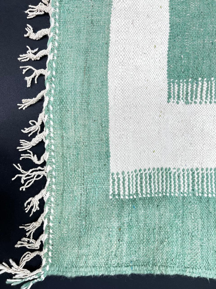 Handmade Moroccan kilim runner rug with green and white geometric block design, minimalist flatwoven hallway rug displayed with Moroccan poufs