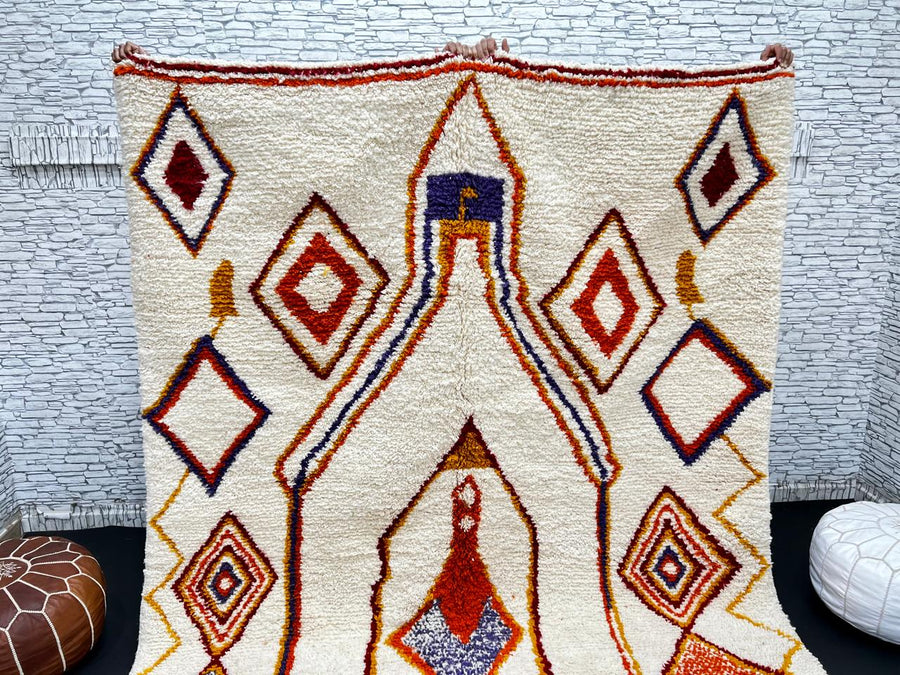 Handwoven Moroccan wool rug with cream background and colorful geometric Berber motifs in orange, yellow, blue, and terracotta