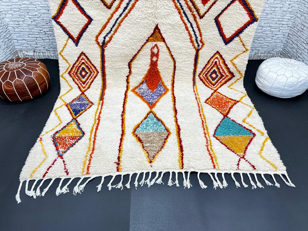 Handwoven Moroccan wool rug with cream background and colorful geometric Berber motifs in orange, yellow, blue, and terracotta