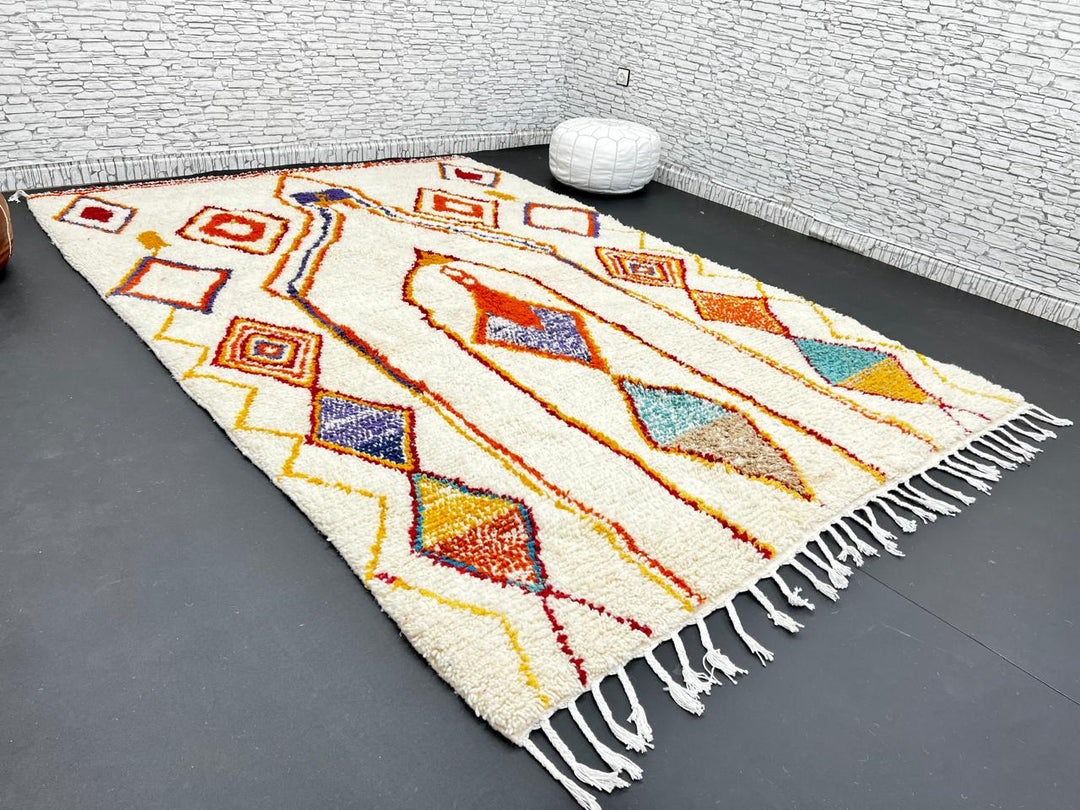 Handwoven Moroccan wool rug with cream background and colorful geometric Berber motifs in orange, yellow, blue, and terracotta
