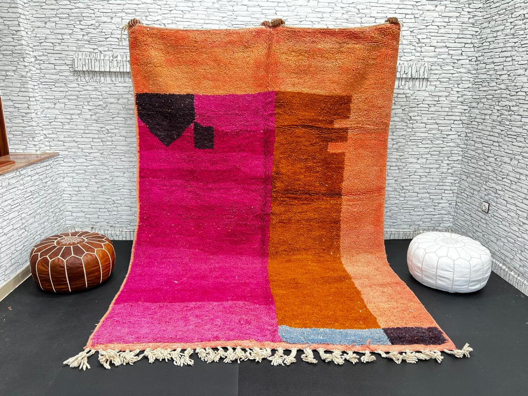 Handwoven Moroccan wool rug in magenta pink and burnt orange color blocks with black and blue accents, fringed ends