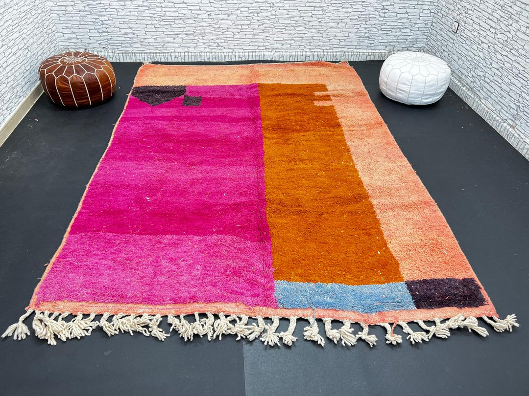 Handwoven Moroccan wool rug in magenta pink and burnt orange color blocks with black and blue accents, fringed ends