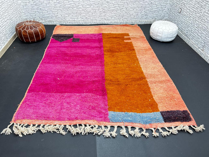 Handwoven Moroccan wool rug in magenta pink and burnt orange color blocks with black and blue accents, fringed ends