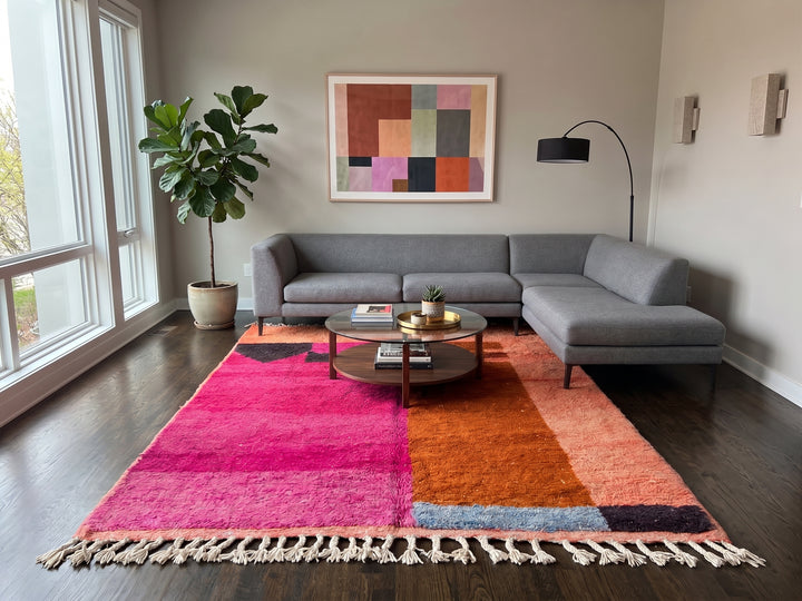 Handwoven Moroccan wool rug in magenta pink and burnt orange color blocks with black and blue accents, fringed ends