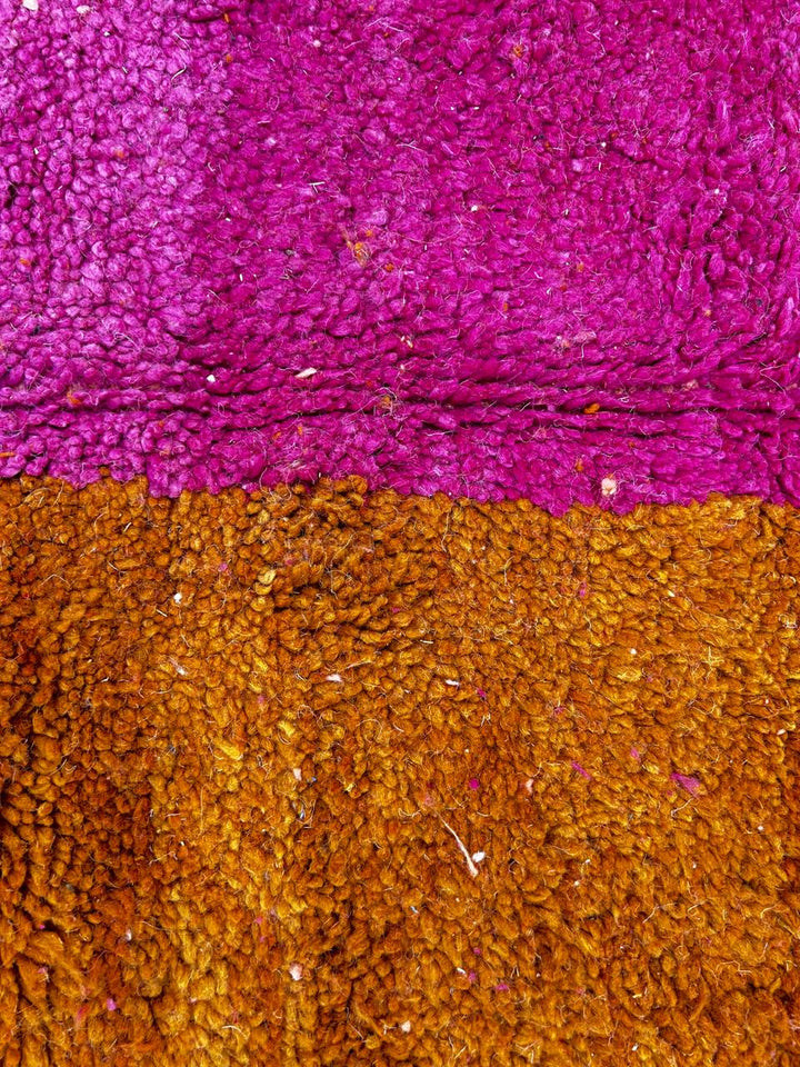 Handwoven Moroccan wool rug in magenta pink and burnt orange color blocks with black and blue accents, fringed ends