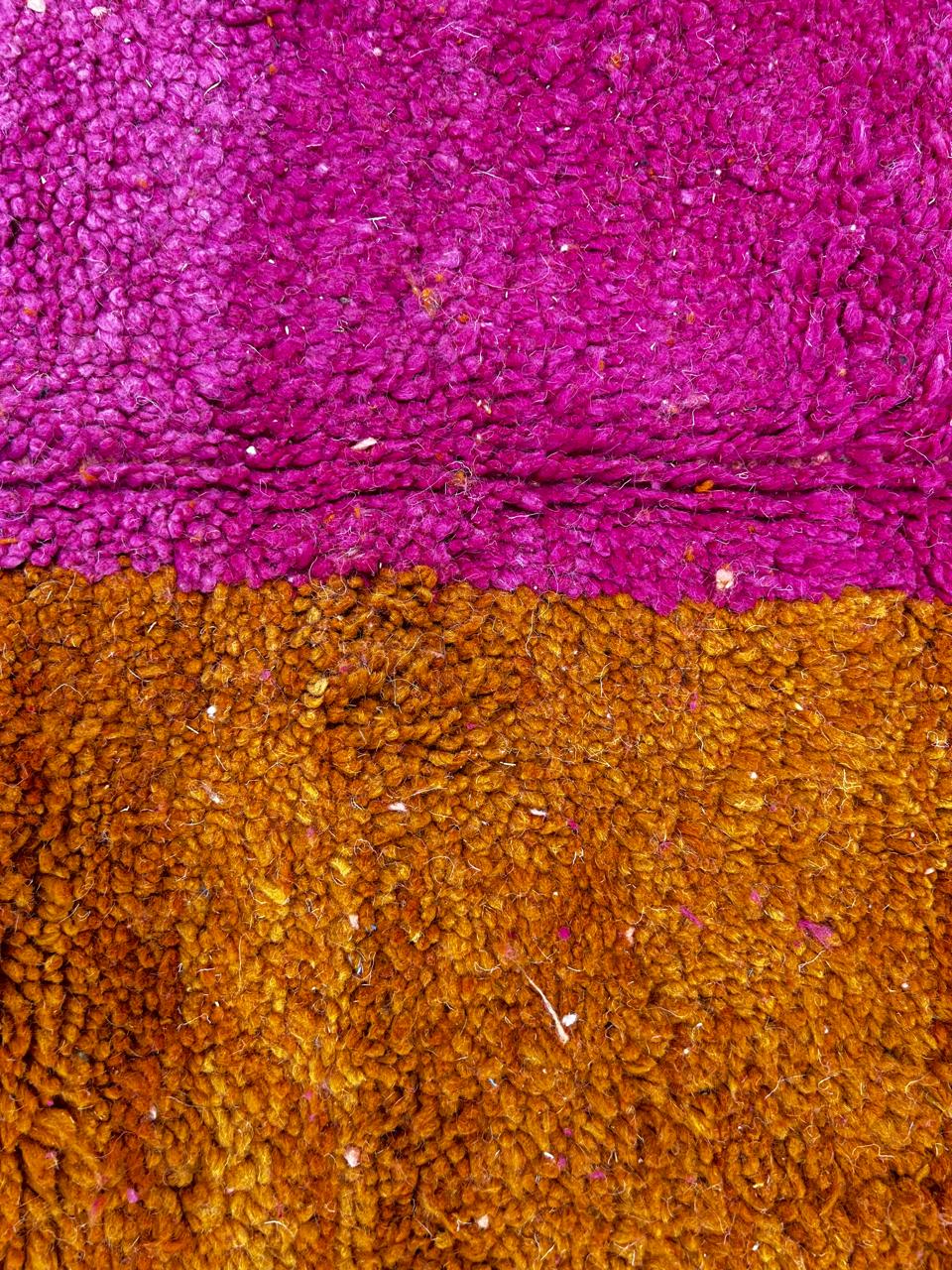 Handwoven Moroccan wool rug in magenta pink and burnt orange color blocks with black and blue accents, fringed ends