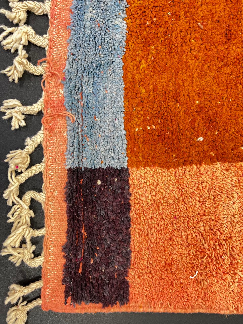 Handwoven Moroccan wool rug in magenta pink and burnt orange color blocks with black and blue accents, fringed ends