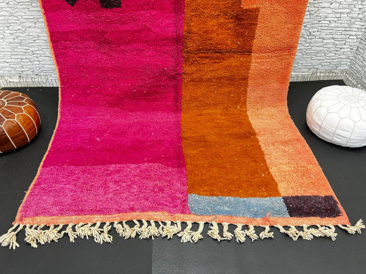 Handwoven Moroccan wool rug in magenta pink and burnt orange color blocks with black and blue accents, fringed ends