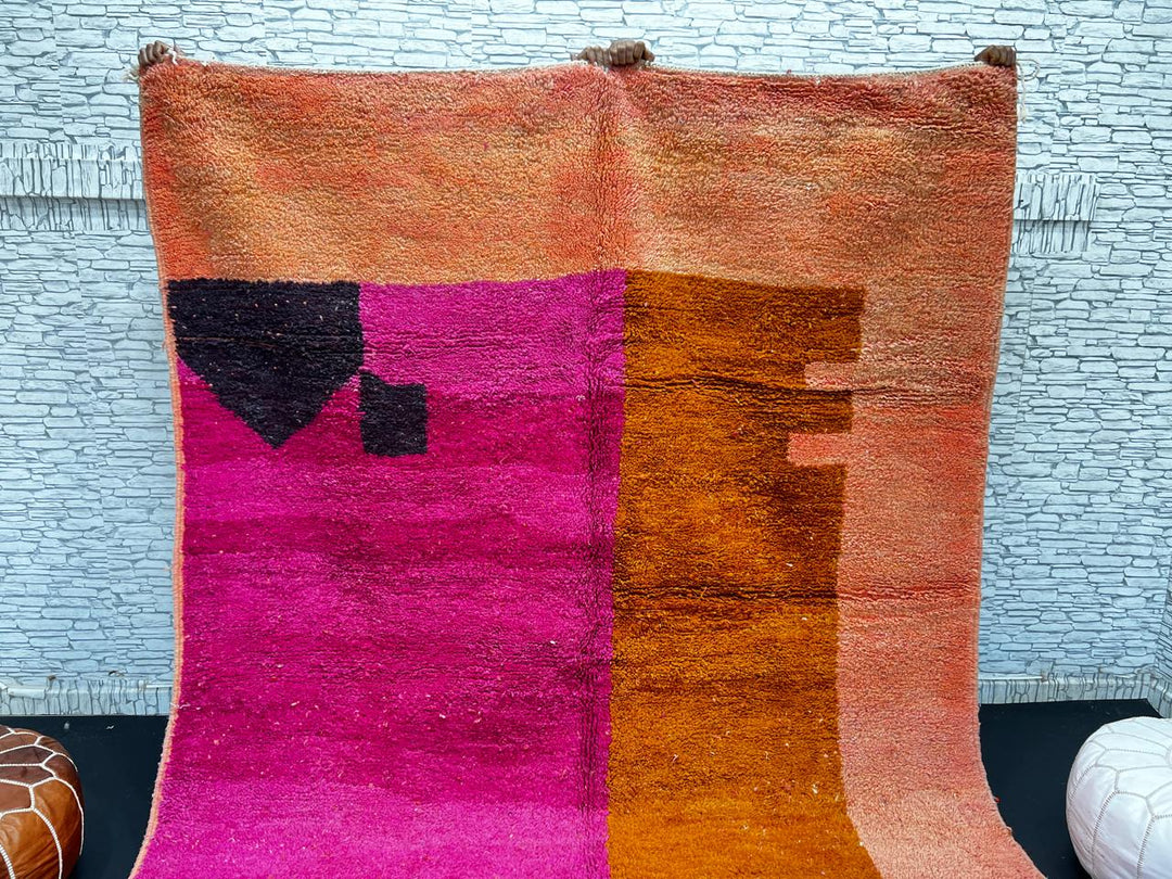 Handwoven Moroccan wool rug in magenta pink and burnt orange color blocks with black and blue accents, fringed ends
