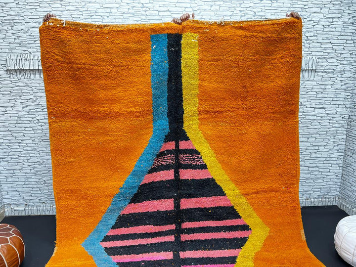 Orange Moroccan wool rug with bold geometric pattern in pink, black, blue, and yellow, handmade by Berber artisans