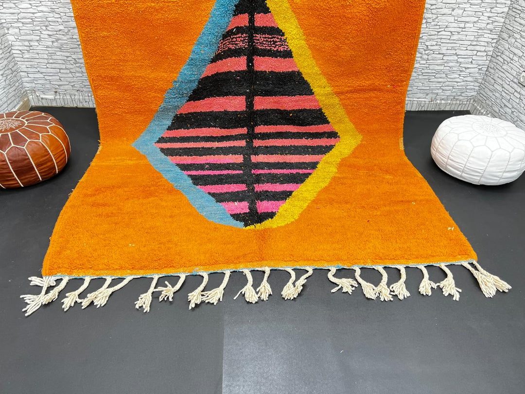 Orange Moroccan wool rug with bold geometric pattern in pink, black, blue, and yellow, handmade by Berber artisans