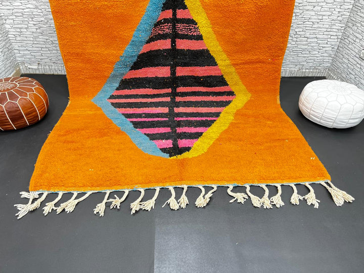Orange Moroccan wool rug with bold geometric pattern in pink, black, blue, and yellow, handmade by Berber artisans
