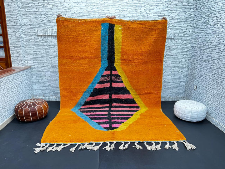 Orange Moroccan wool rug with bold geometric pattern in pink, black, blue, and yellow, handmade by Berber artisans