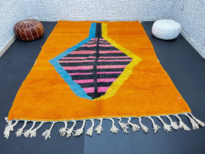 Orange Moroccan wool rug with bold geometric pattern in pink, black, blue, and yellow, handmade by Berber artisans