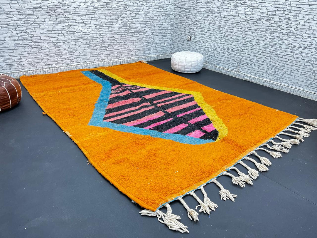 Orange Moroccan wool rug with bold geometric pattern in pink, black, blue, and yellow, handmade by Berber artisans