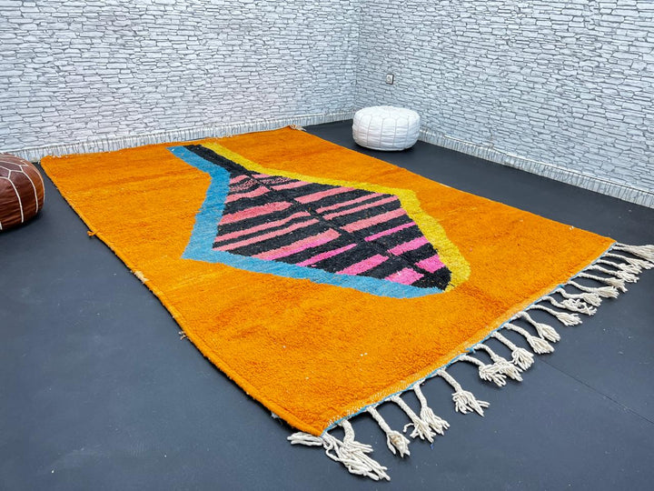 Orange Moroccan wool rug with bold geometric pattern in pink, black, blue, and yellow, handmade by Berber artisans