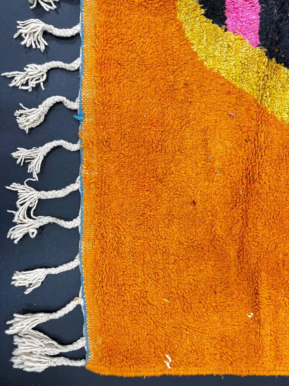 Orange Moroccan wool rug with bold geometric pattern in pink, black, blue, and yellow, handmade by Berber artisans