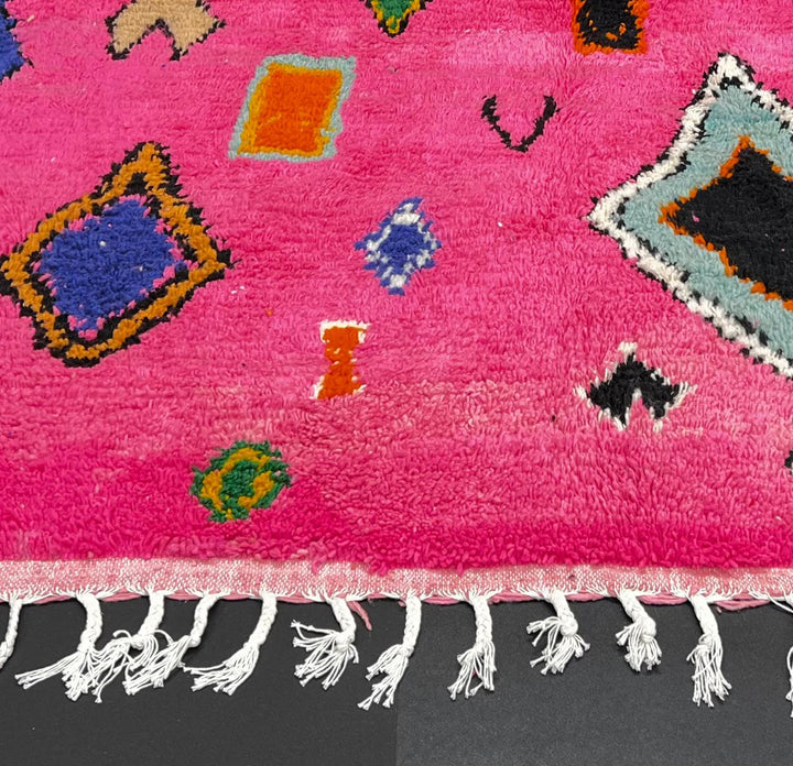 Handmade pink Moroccan runner rug with colorful geometric Berber motifs in green, blue, orange, yellow, and black.