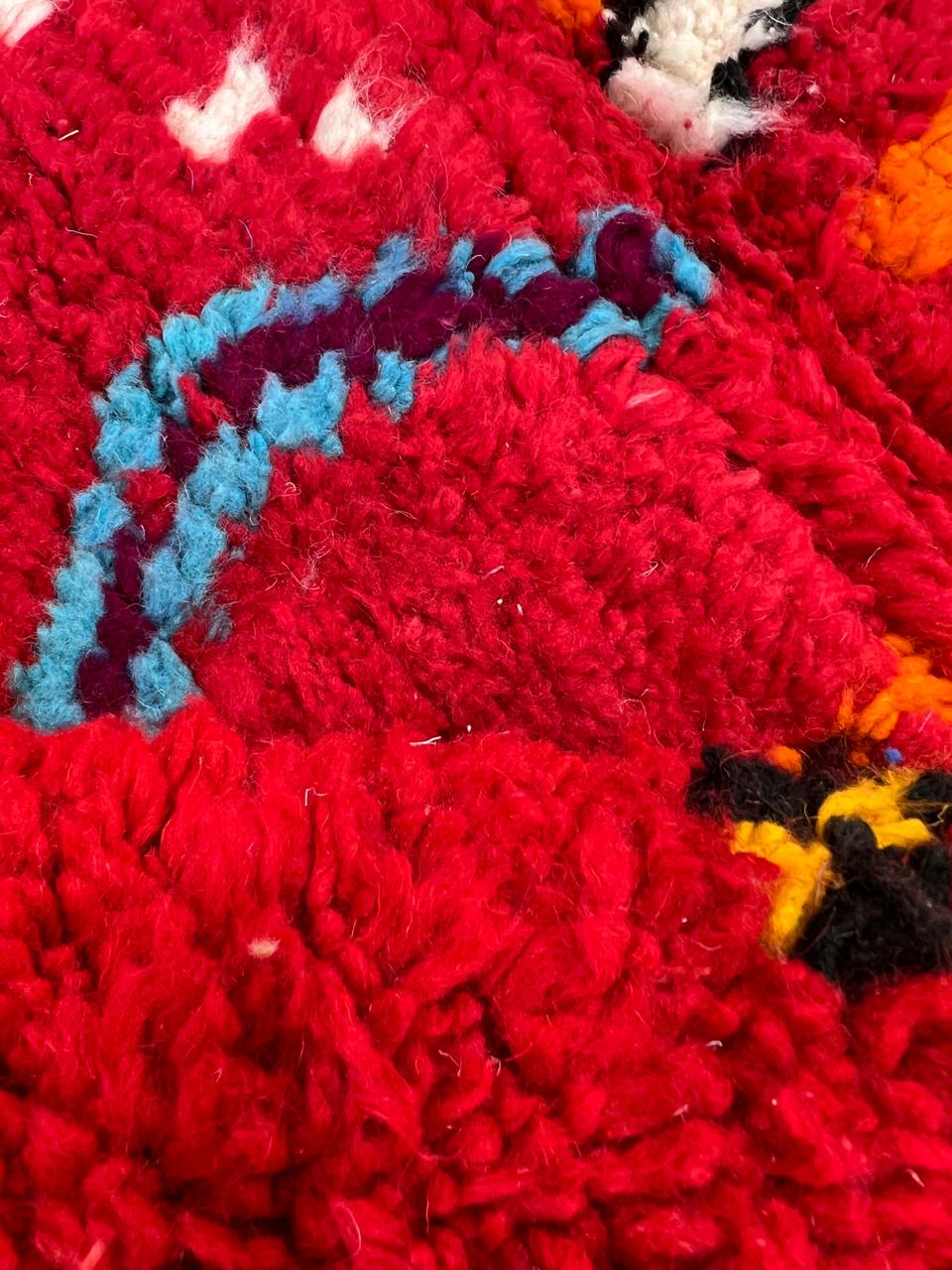 Round handmade Moroccan Berber rug with deep red wool base and colorful tribal geometric symbols.