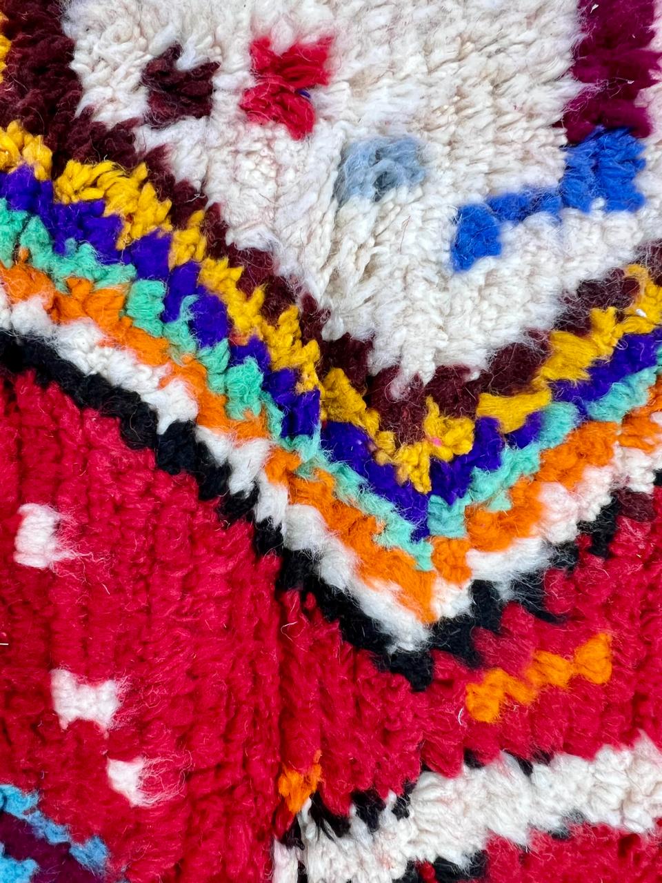 Round handmade Moroccan Berber rug with deep red wool base and colorful tribal geometric symbols.