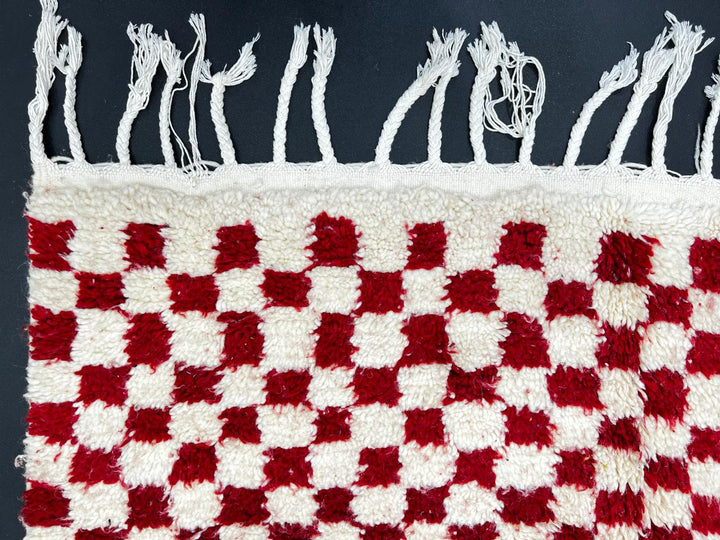 Red and white checkerboard Moroccan runner rug made of handmade wool with fringed ends on white background